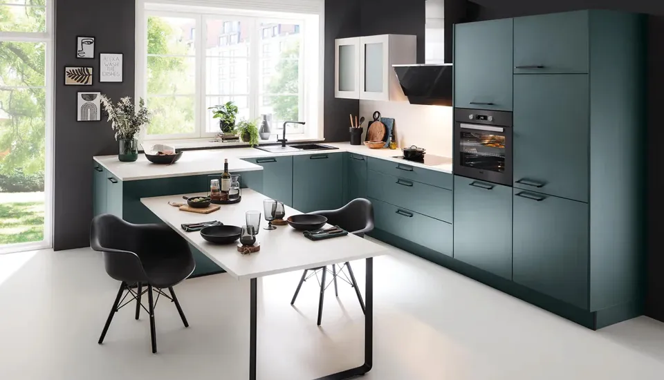 Designorientierte Küche in dunklem Grün mit integriertem Esstisch, großen Fenstern und kontrastreicher Wandgestaltung, ideal für moderne Wohnküchen mit urbanem Charme.